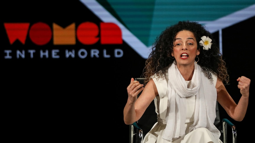 Woman sits on stage speaking emphatically 