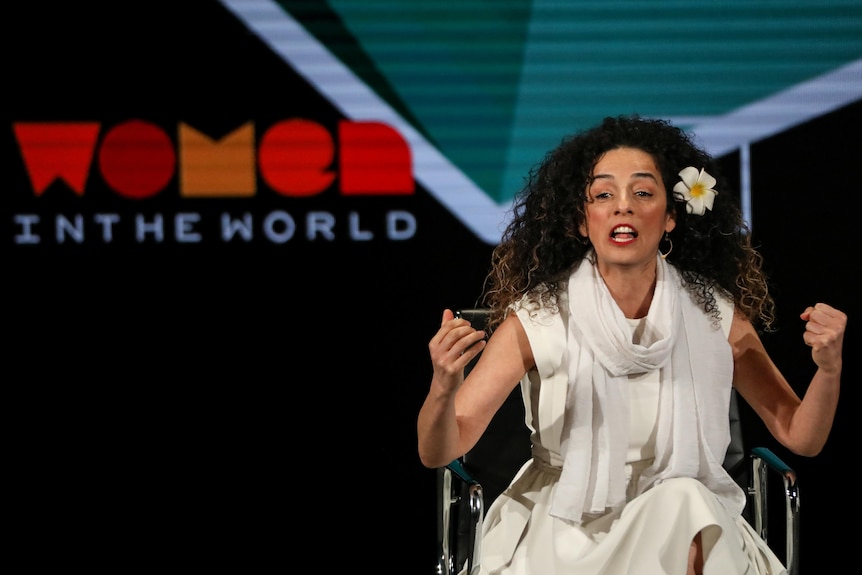 Woman sits on stage speaking emphatically 