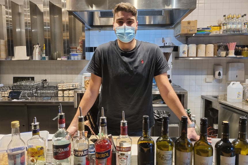 man stands behind a bar while wearing a face mask