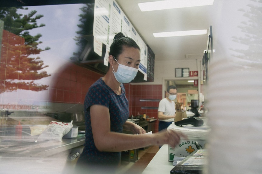 Susan Hhi works in her fish and chip shop, as a reflection of the beach can be seen