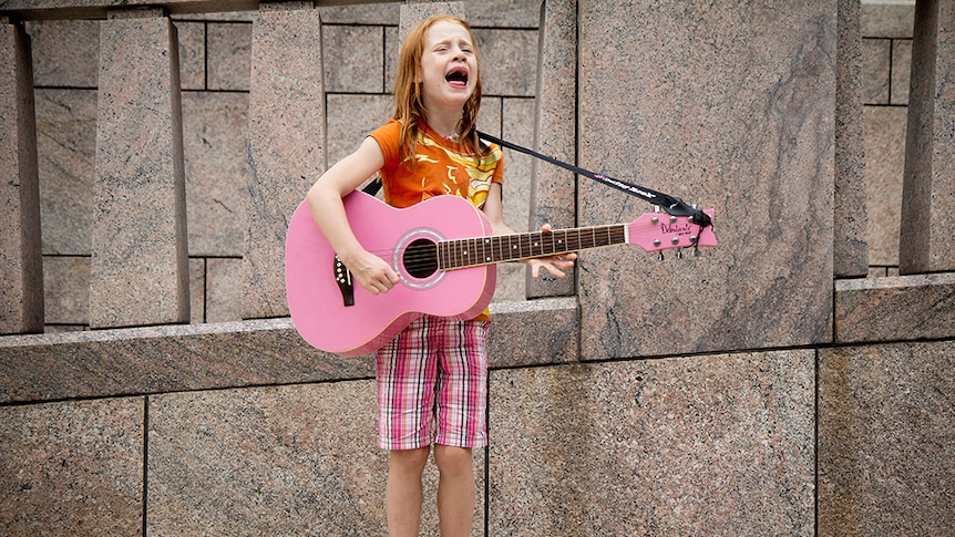 A child sings and plays a pink guitar