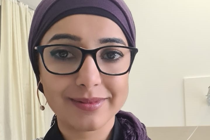 Dr Panhwar wears glasses and a purple head scarf and sits in her consultation room