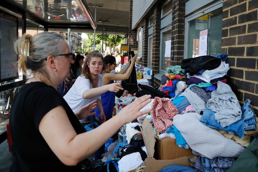 Women sort through piles of clothing stacked on tables outside a building