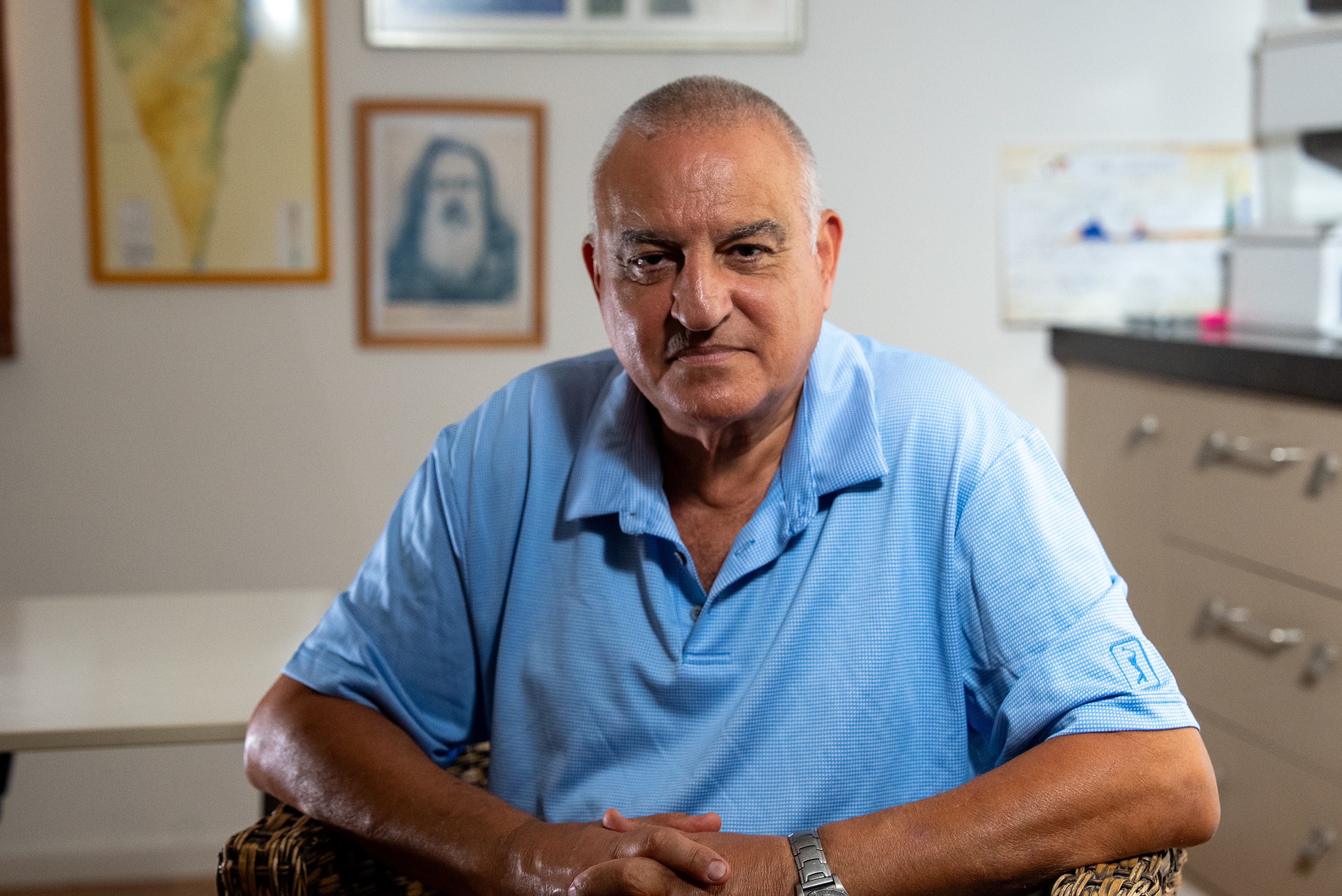 Gabi Siboni wears a blue polo top as he sits with interlanced hands on his lap and looks at the camera.