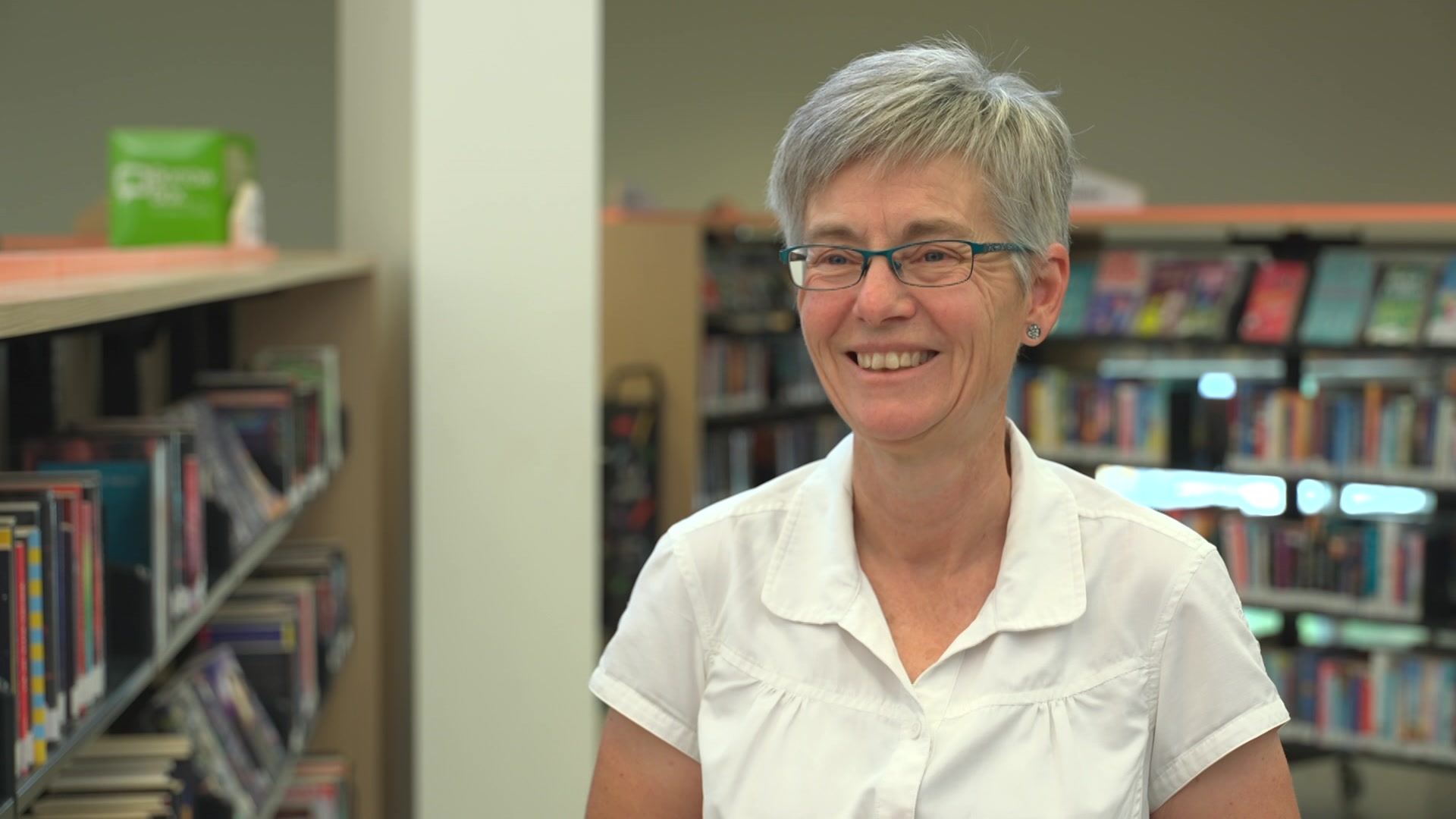 A woman smiles standing next to book shelves