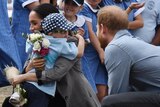 Prince Harry watching a young boy hug his wife.