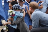 Prince Harry watching a young boy hug his wife.