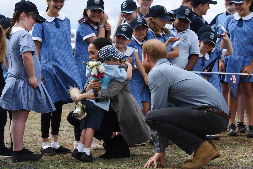 Prince Harry watching a young boy hug his wife.