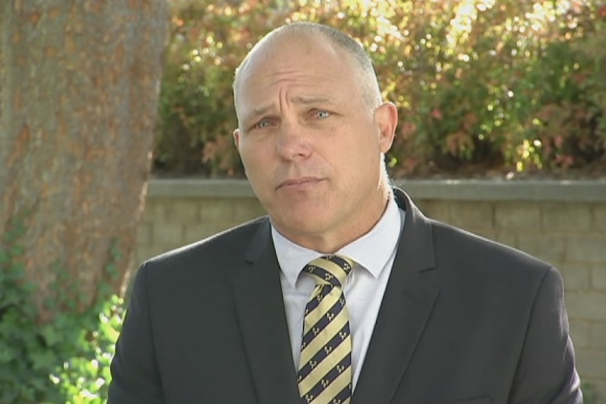 A man in a suit and tie speaks to cameras.