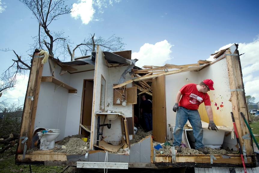 A man picks up debris in a tornado-damaged home