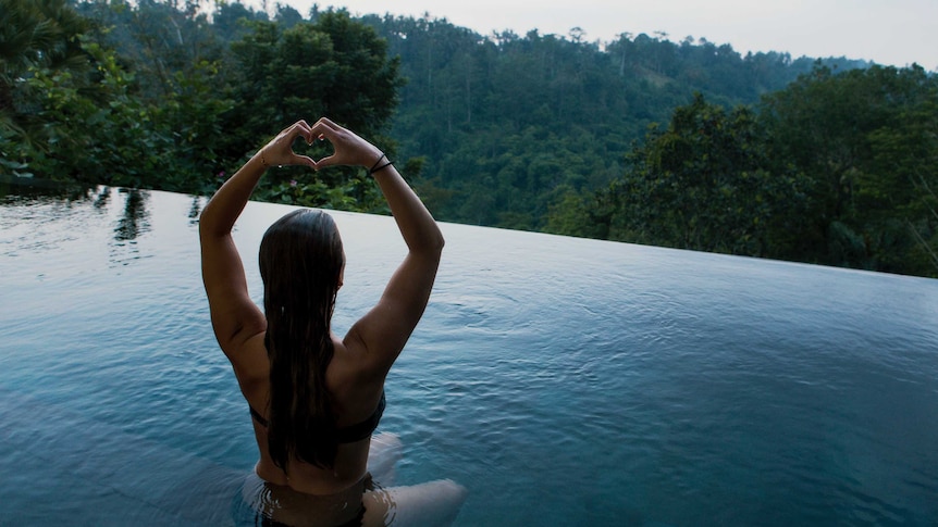 Woman sitting in a pool making a love heart symbol with her hands.