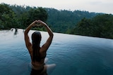 Woman sitting in a pool making a love heart symbol with her hands.