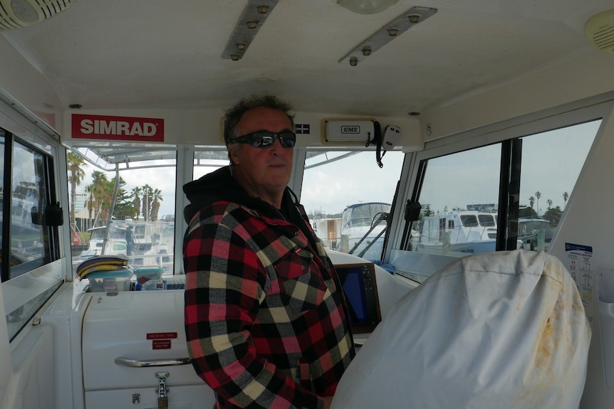A man on a boat standing at the steering wheel.
