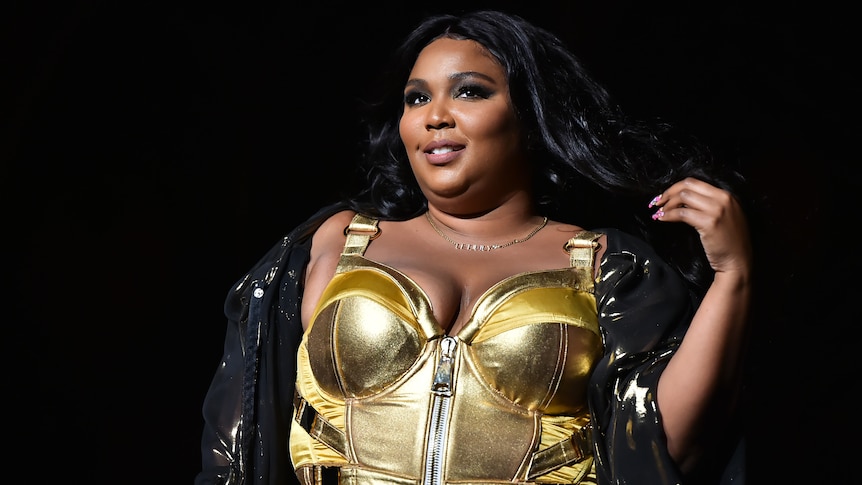 Lizzo smiling and wearing a gold top
