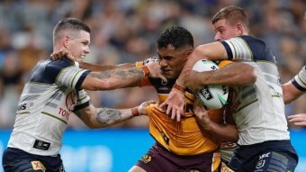 An NRL player tries to fend off two tacklers.