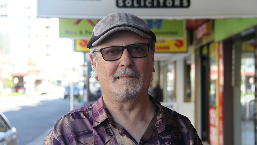 Older man with hat and glasses on standing in street.