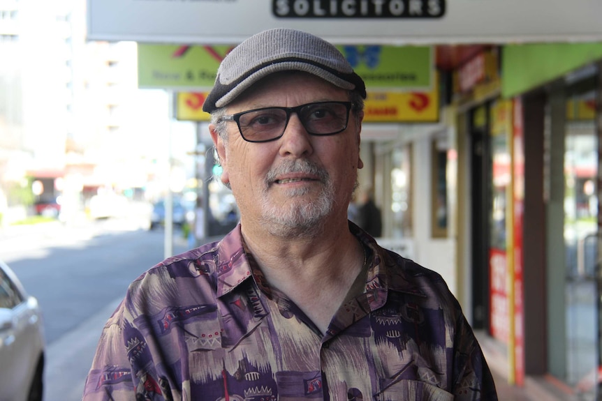 Older man with hat and glasses on standing in street.