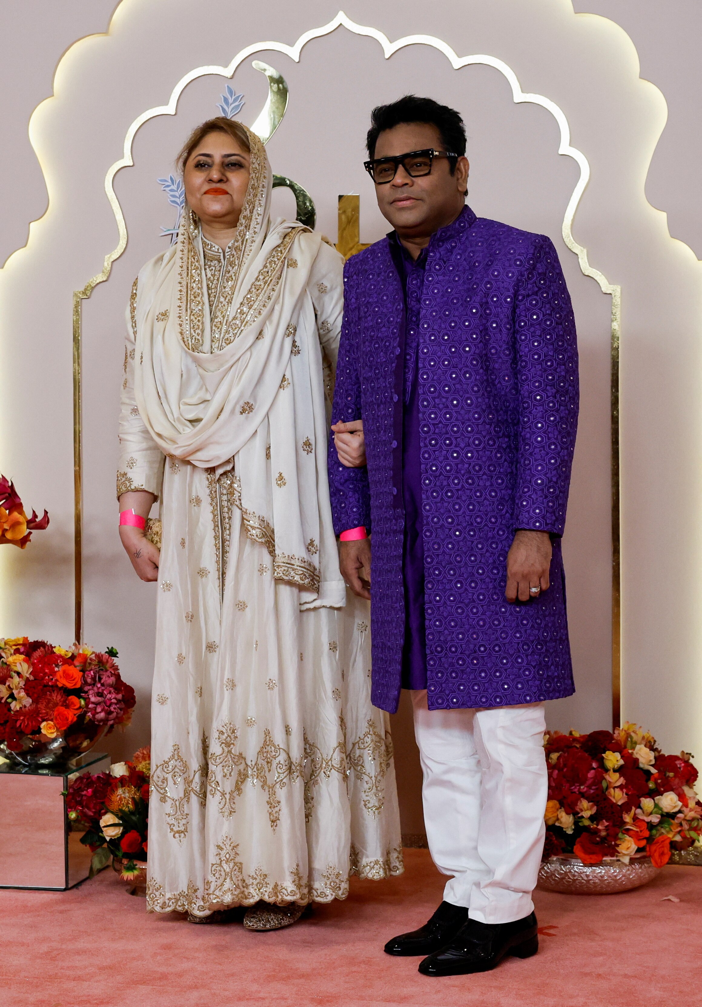 Saira Banu wears a white gown with gold embellishments and AR Rehman wears a purple tunic with white pants