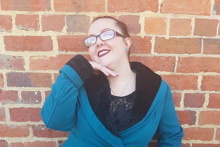 Jasmine Carrington poses in front of a brick wall in a blue coat