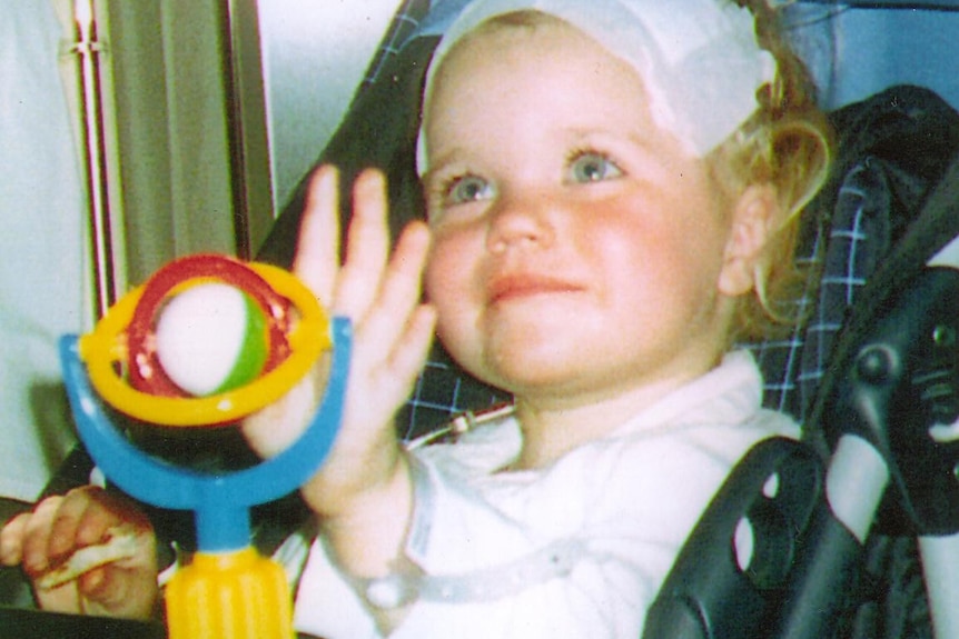 Siahn has a bandage on her head looking up from a pram smiling