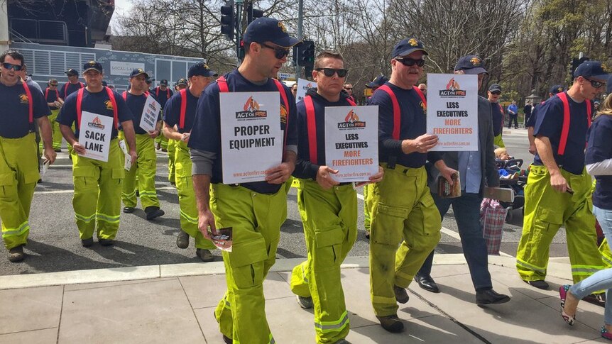 Firefighters walking in a group protest in Canberra, holding signs.