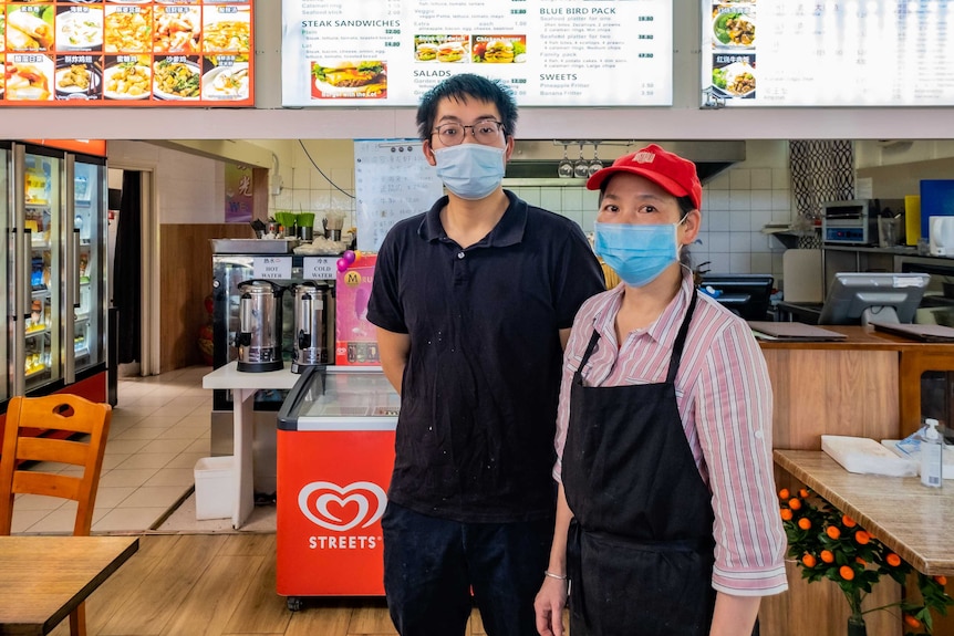 A man and a woman in surgical face masks standing in a fish and chip shop