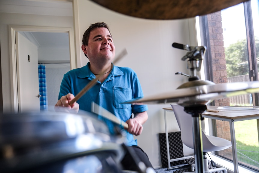 Conor is captured while playing his drumkit. It’s a midshot, taken in between a drum and a cymbal. He is wearing a blue shirt.