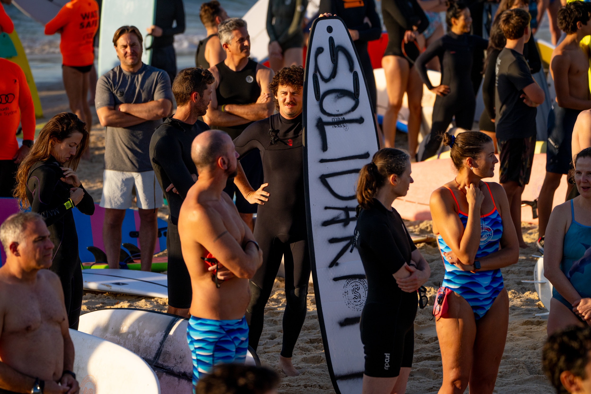 La gente espera en la playa a que Bondi salga a remar, una tabla de surf está pintada con spray solidario