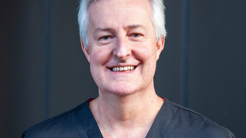 A smiling man wiith neat grey hair, wearing medical scrubs.