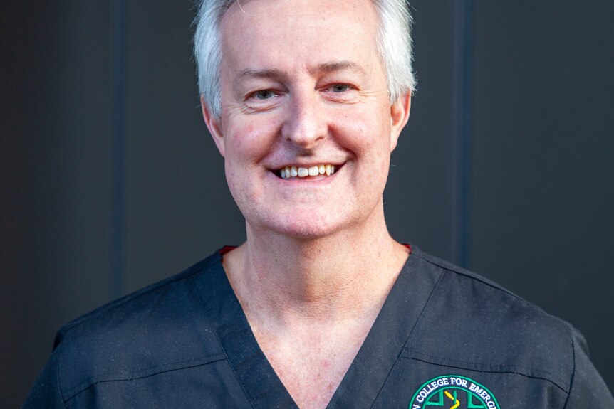 A smiling man wiith neat grey hair, wearing medical scrubs.