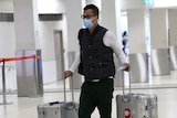 A man wearing a mask carrying luggage at Perth Airport.