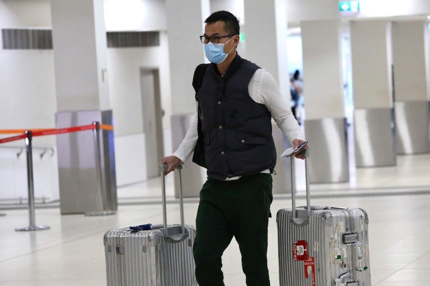 A man wearing a mask carrying luggage at Perth Airport.