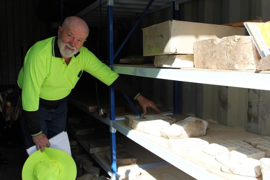 Man in high vis shirt stands beside shelves with chunks of rock