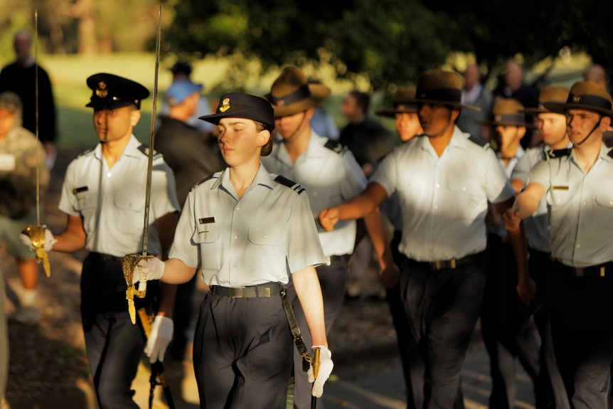 A female Australian Airforce cadet marches in a parade with others holding a sword. 