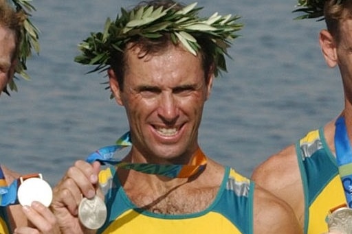 A man with a wreath on his head stands on a podium with a medal