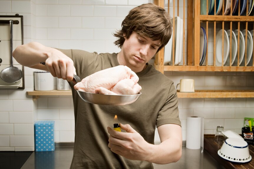 A man with a raw chicken considers his cooking options
