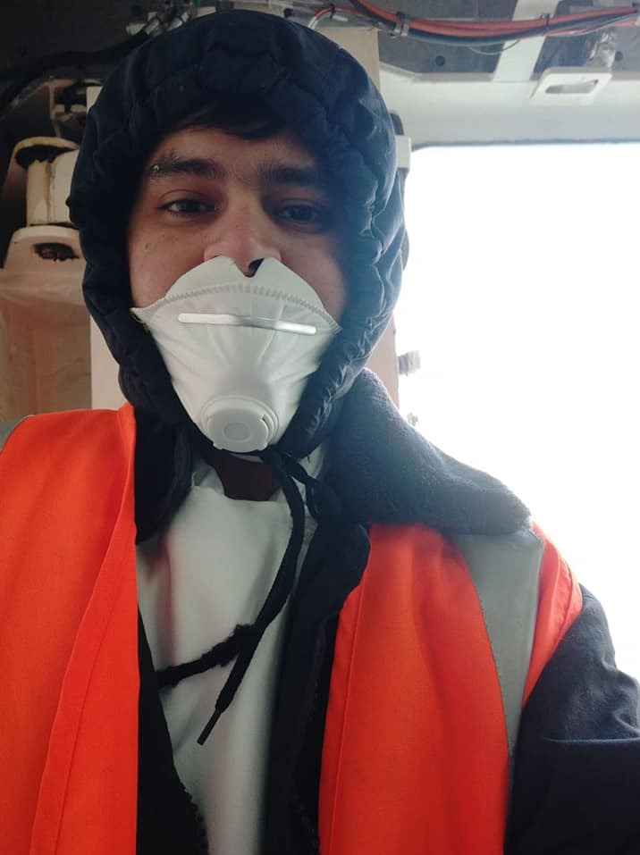 A man in a p2 facemask, hoodie and high-vis vest standing on the dock of a ship