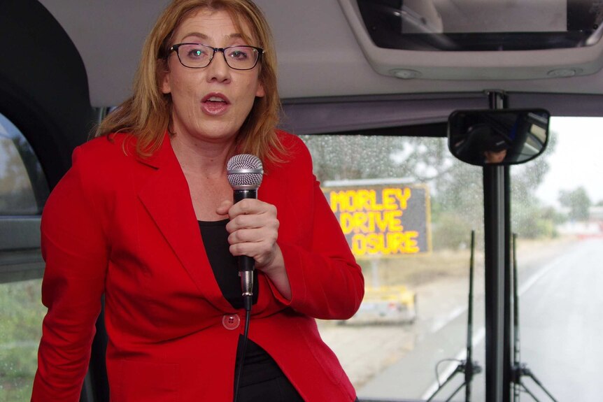 Opposition transport spokeswoman Rita Saffitoti playing tour guide on a bus trip holding a microphone.