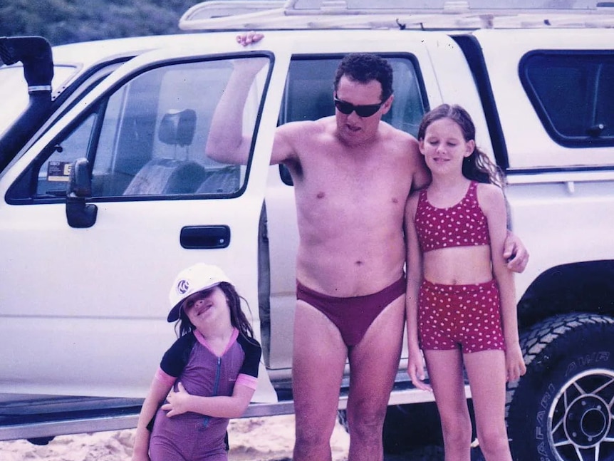 Une vieille photo de famille d'un père et de ses enfants debout près de la voiture à la plage 