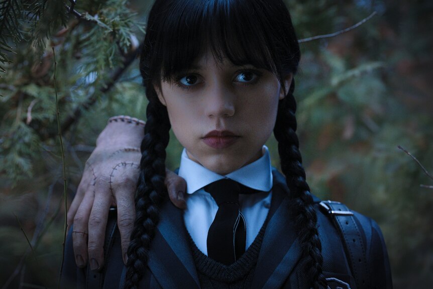Wednesday Addams looks at camera with hand The Thing on her shoulder - television still
