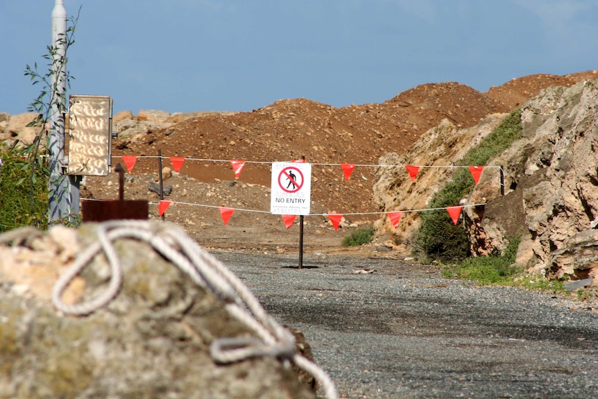 A sign says 'Asbestos no entry' hung on orange warning flags across the worksite's entrance.