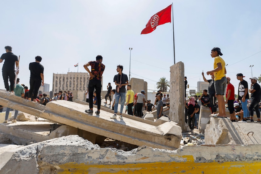 Hombres parados sobre escombros con una bandera ondeando en el fondo y un palacio en el fondo