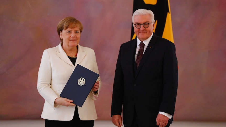 Angela Merkel holds her certificate of appointment and stands next to President Frank-Walter Steinmeier.