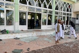 Man stands in front of mosque with shattered windows 