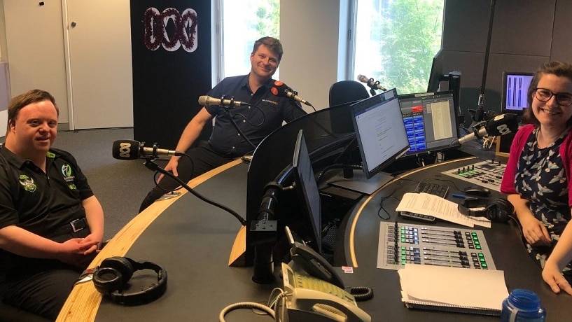 Two men sit on one side of the radio desk, female presenter sits on the other side.