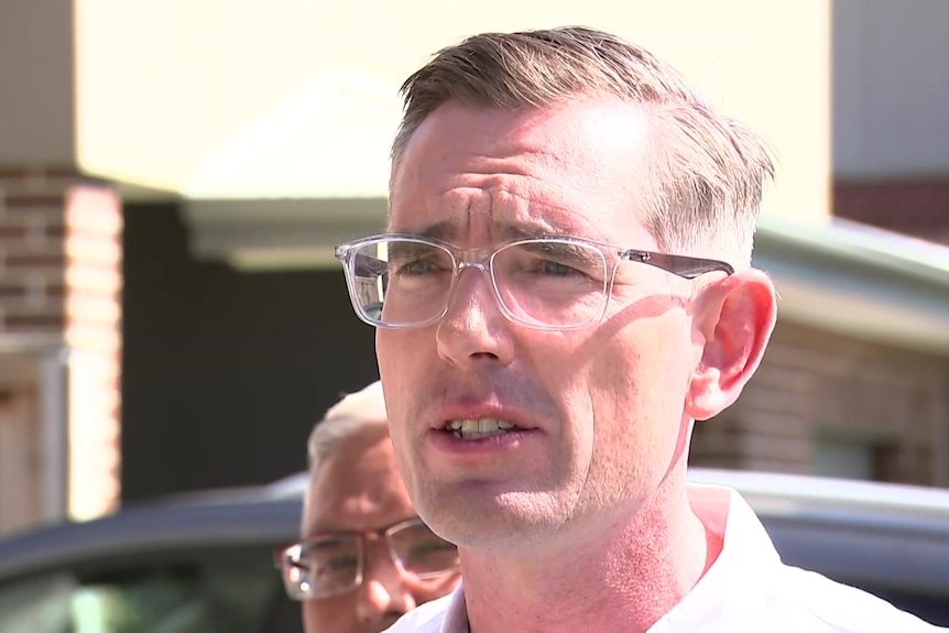 Man with glasses talking to the media outdoors