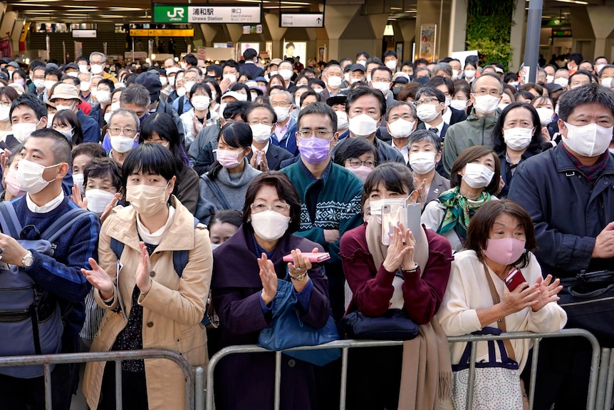 A crowd of people outside a Japanese train station wearing masks.