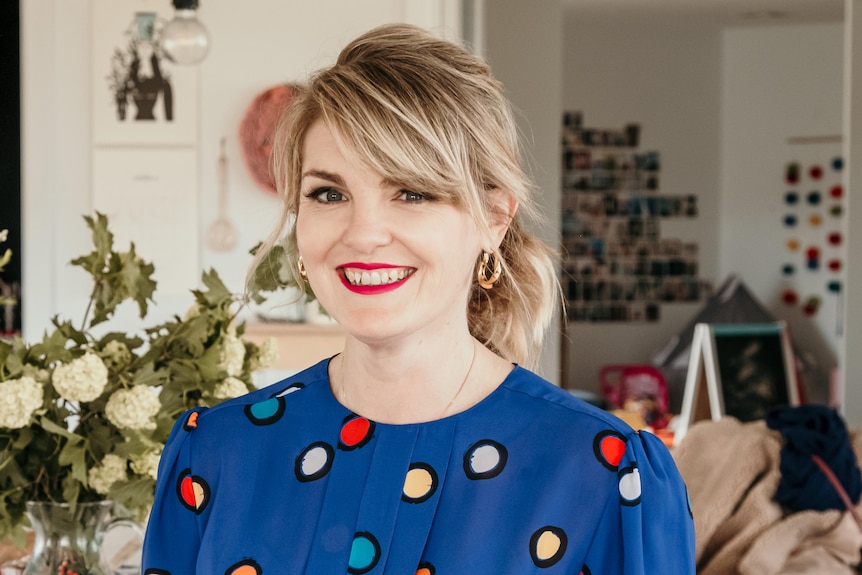 A woman with blonde hair and a bright blue shirt, smiling.