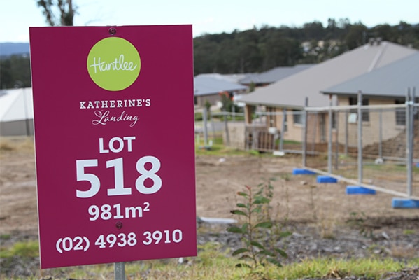 A sign advertising a development lot in Huntlee, with a half-built house in the background