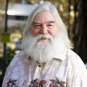 A man with long white hair and beard smiles at the camera.